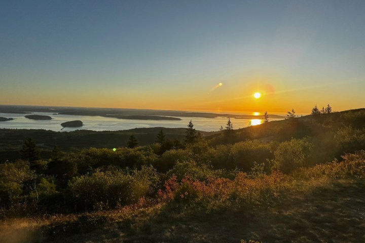 Sunset over a landscape with trees and distant water, clear sky.