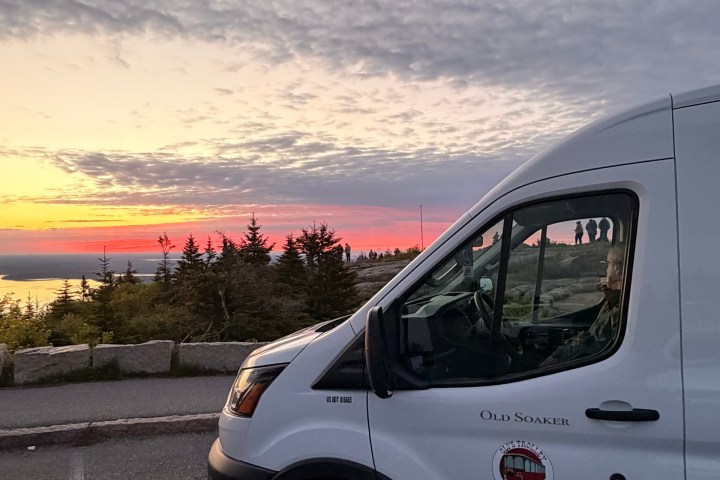 White van parked by a scenic sunset view with clouds and trees.