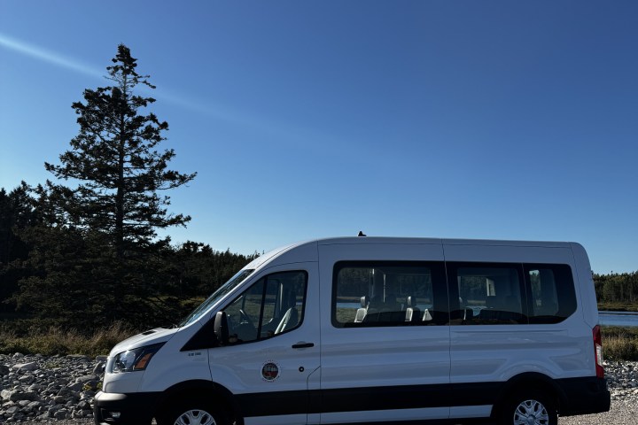 White van parked by a tree and a rocky area under a clear blue sky.