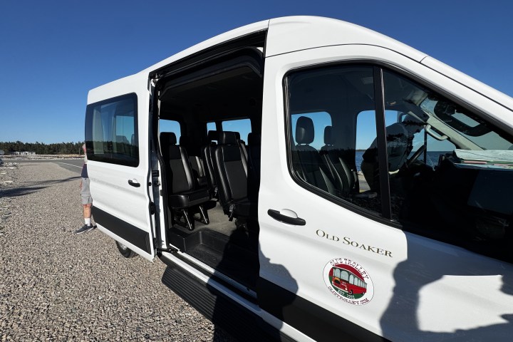 White passenger van with sliding door open on gravel surface.